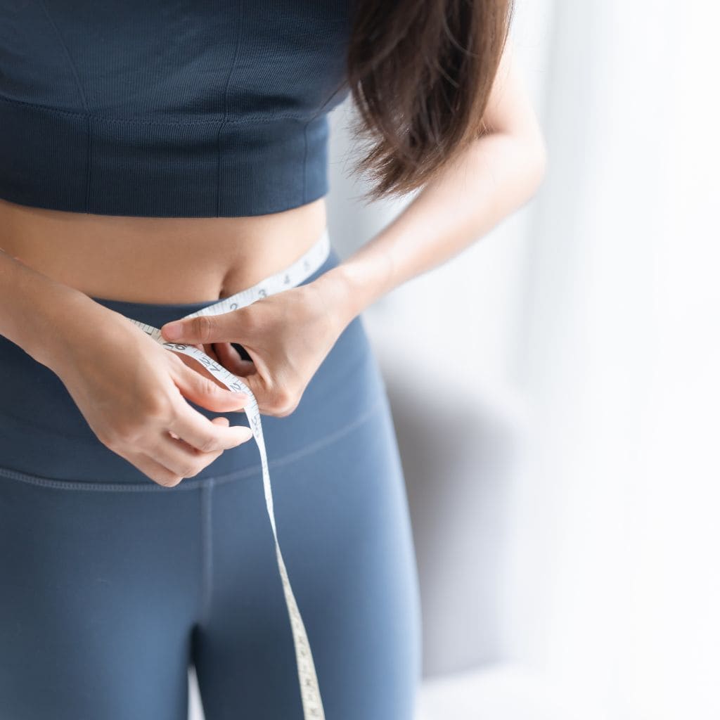 Mujer midiendo su cintura con cinta métrica para controlar grasa corporal antes de tratamientos estéticos reductores